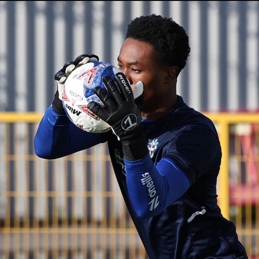 Person wearing goalkeeper gloves holding a soccer ball with a blurred background